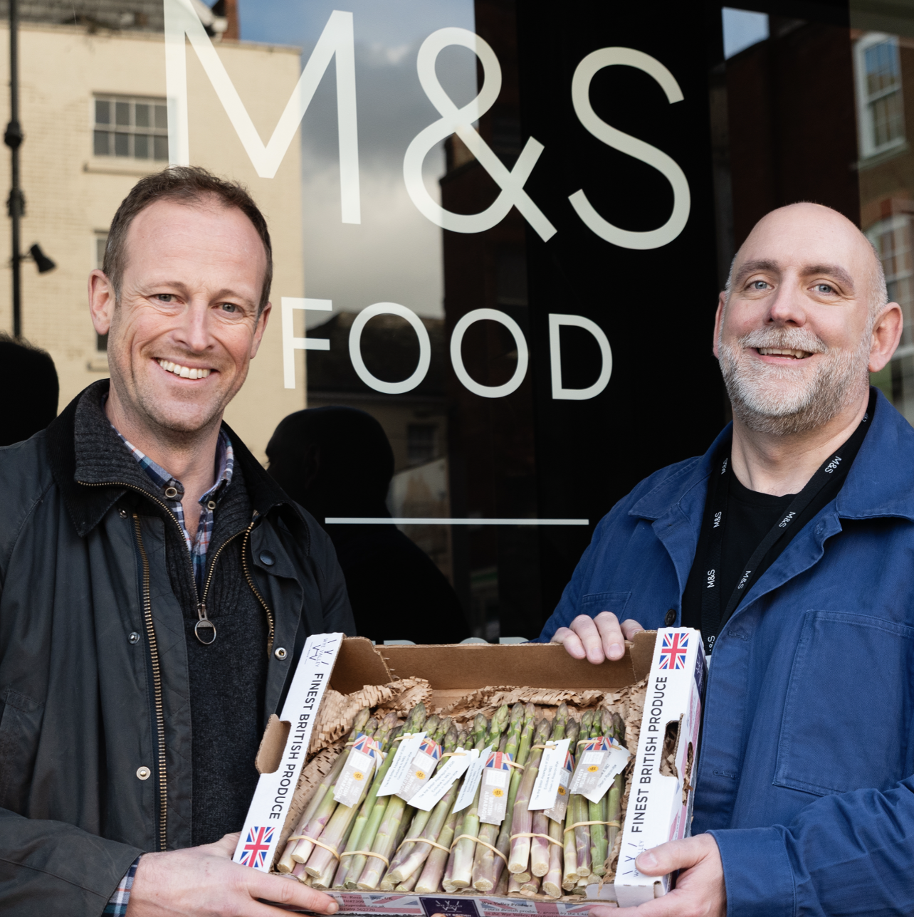 two people holding a box of asparagus and smiling at the camera