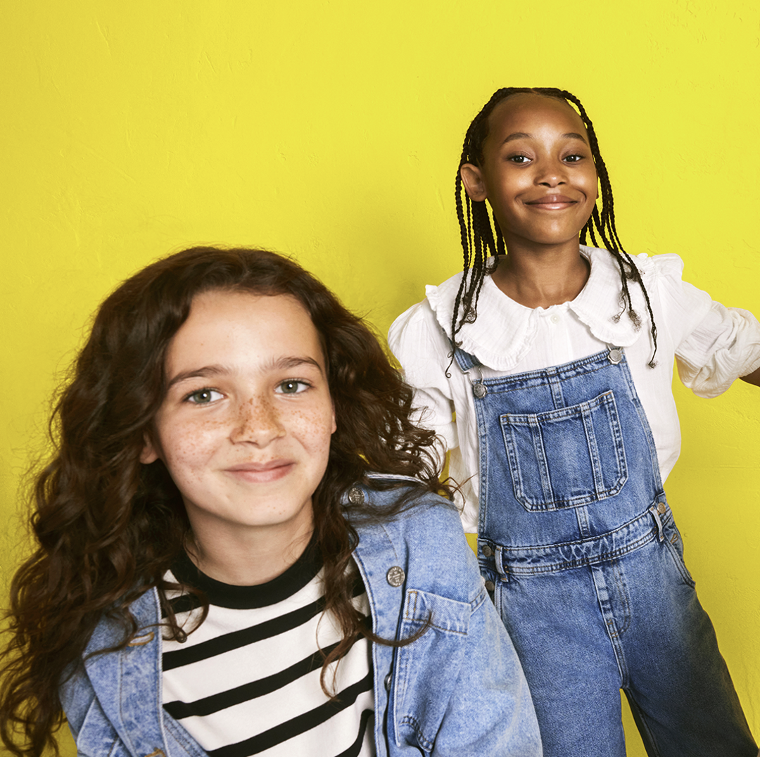 two children in front of a yellow background smiling at the camera
