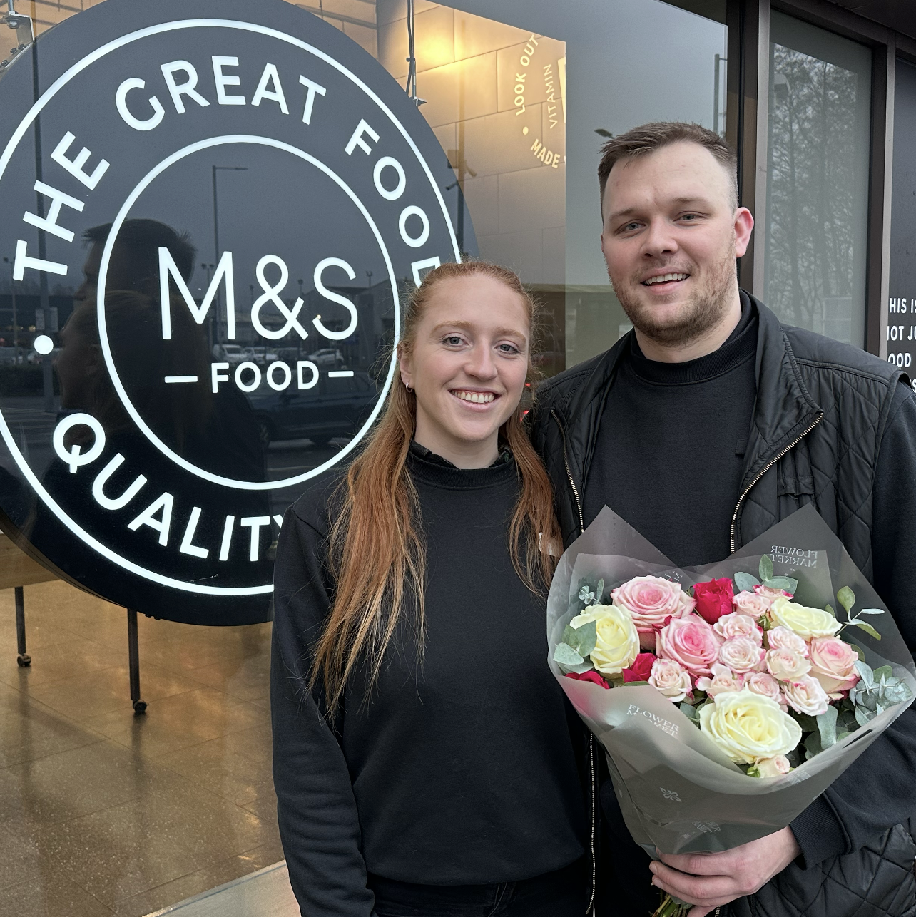 two people smiling at the camera and holding a bouquet of flowers