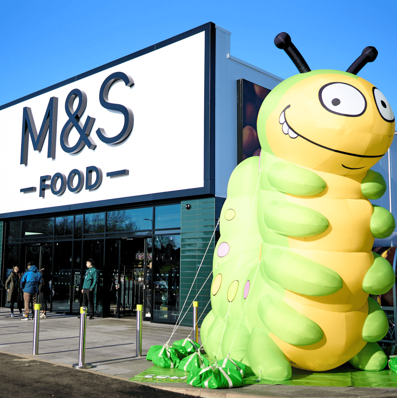 a blow up Colin the caterpillar mascot next to an M&S food store