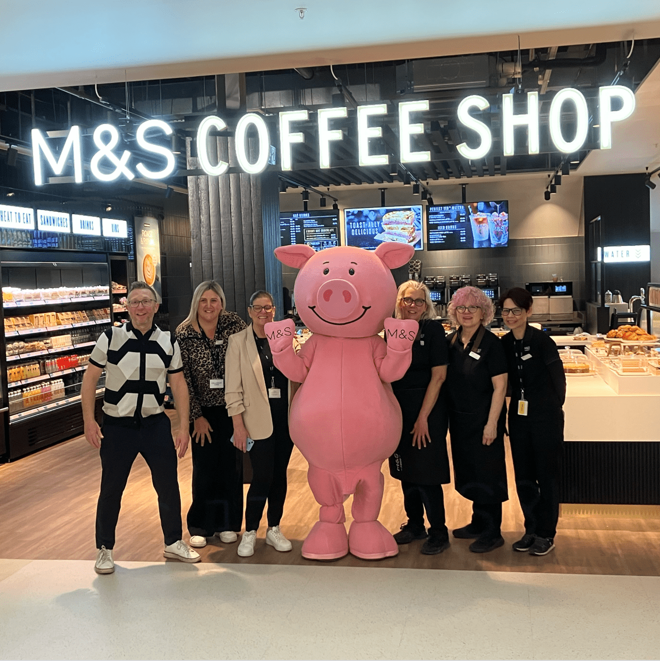 A group of people standing with a person in a pink pig mascot costume