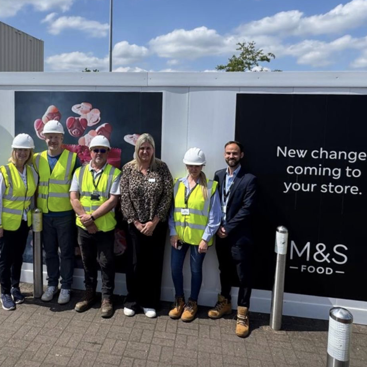 A group of people in high vis jackets and hard hats outside a building site