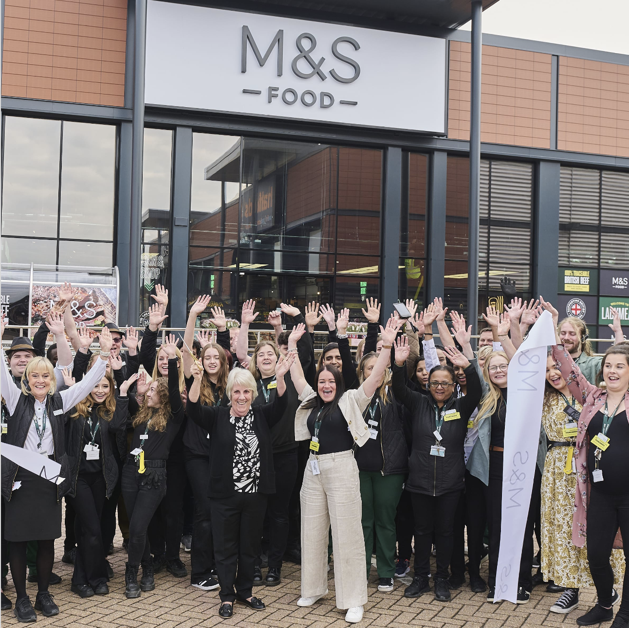 A crowd of people standing in front of a Marks & Spencer store cheering
