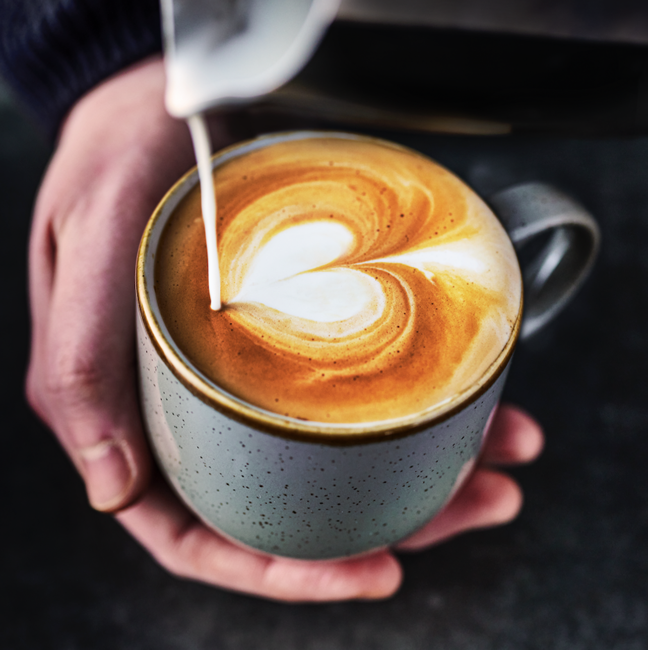 A person pouring a coffee with foam art in a heart shape