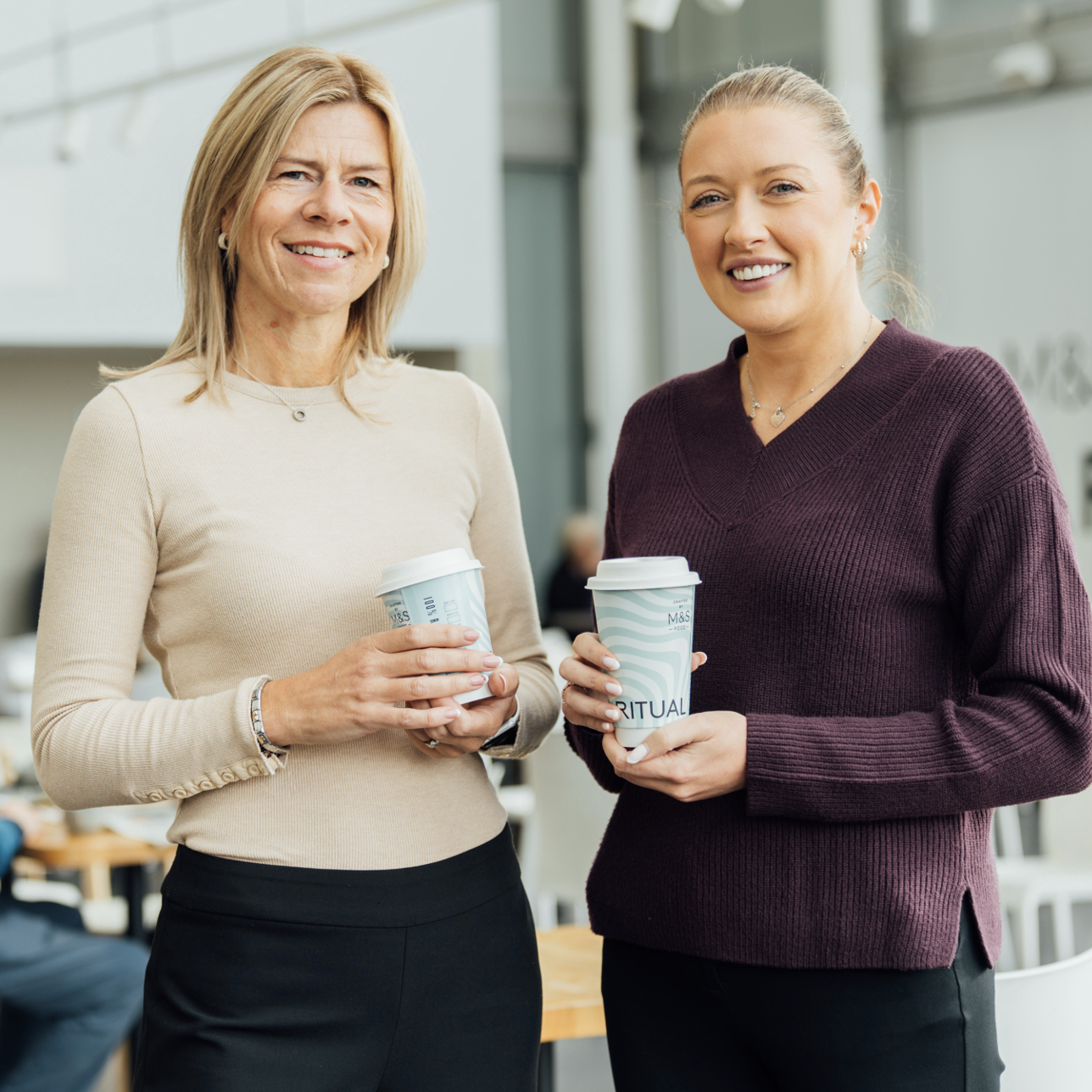 Two people holding M&S coffee cups and smiling