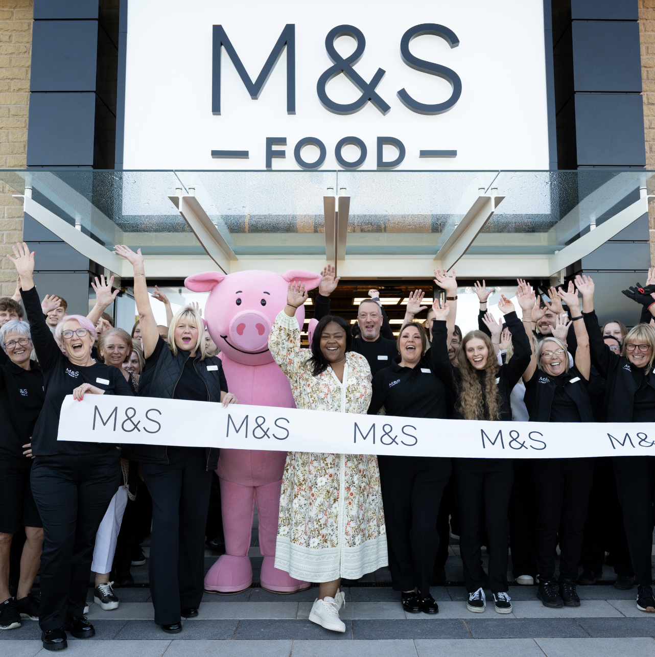 a group of people and a pig mascot outside an M&S store cheering
