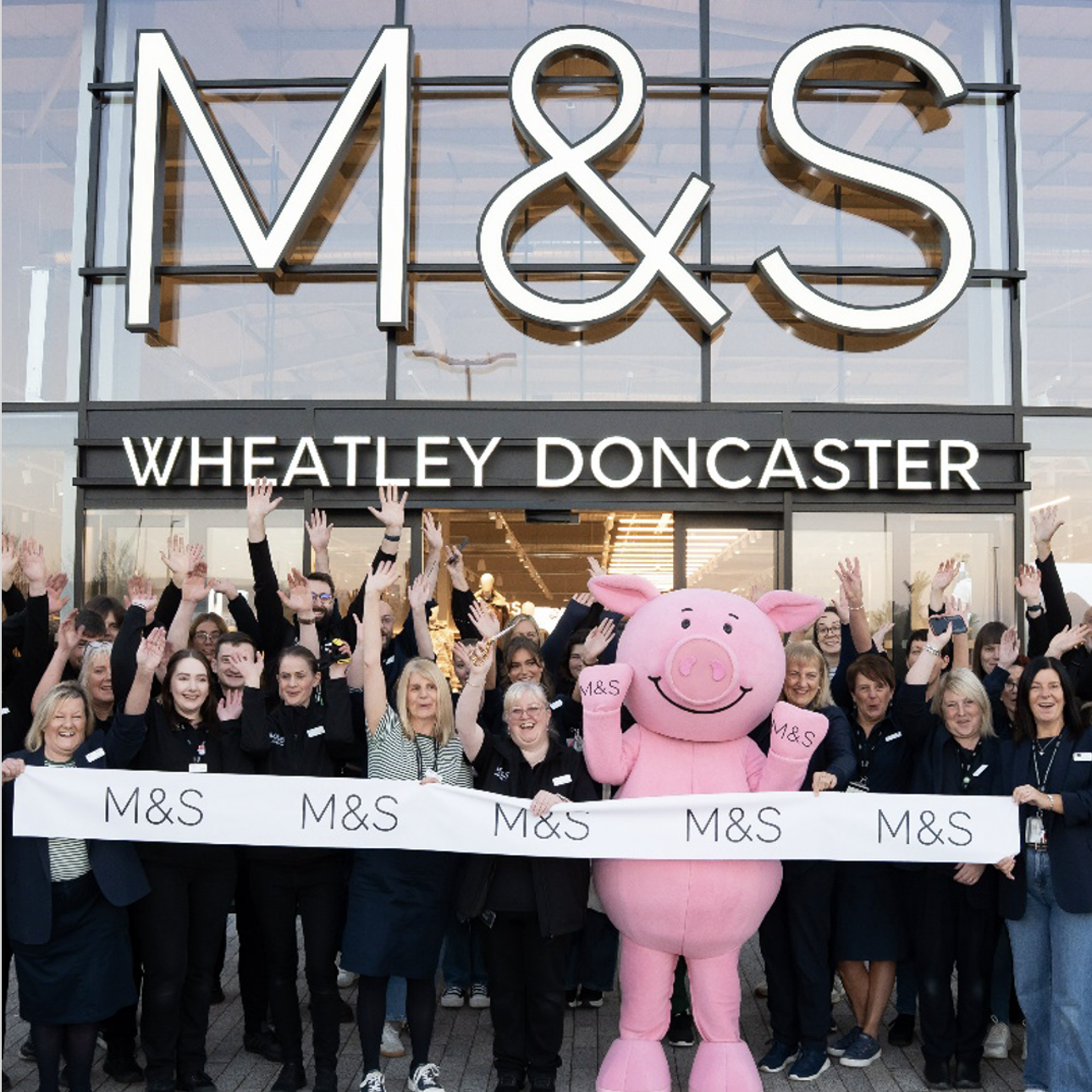a group of people in front of an M&S store with a person in a pig mascot costume