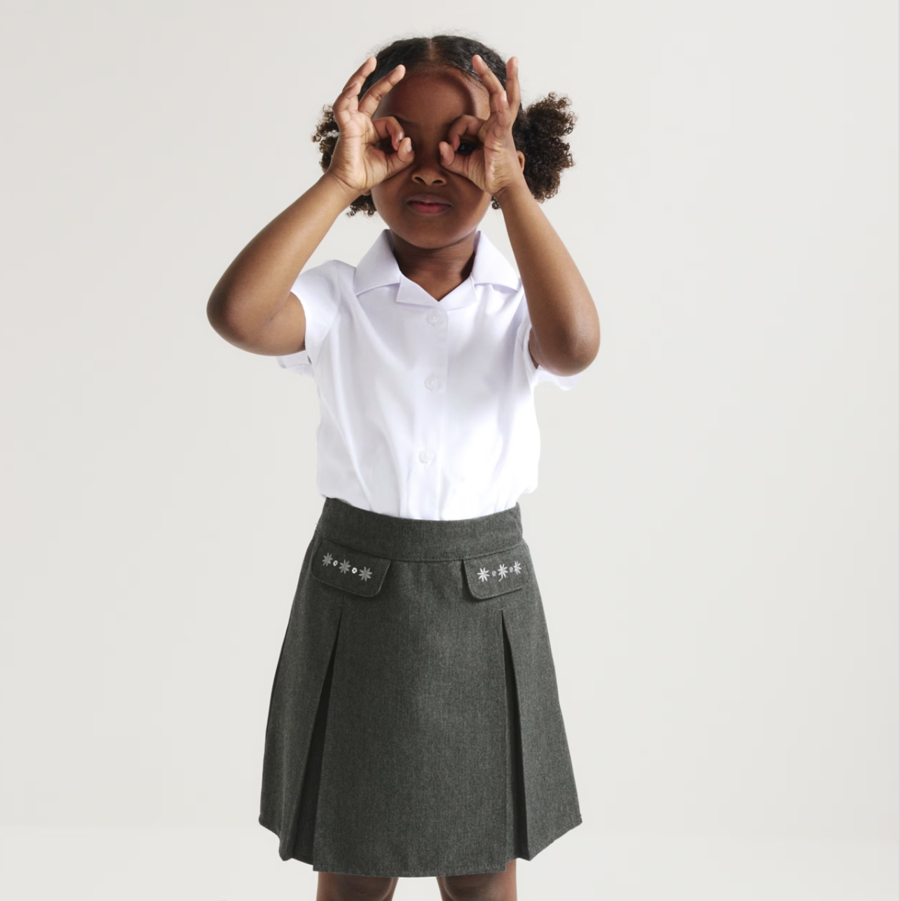 a child wearing a great pleated skirt and white polo shirt
