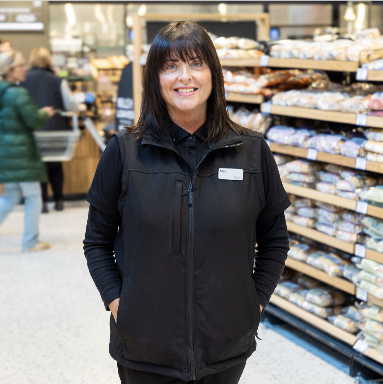 a person standing in a supermarket wearing an all black outfit and smiling at the camera