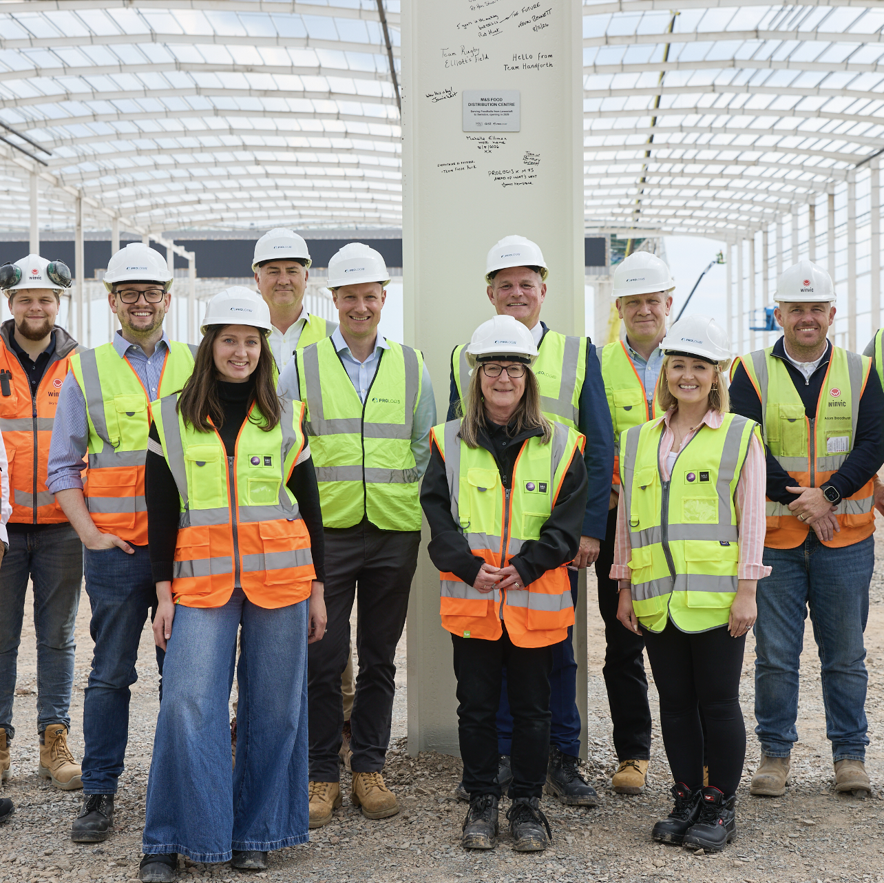 a group of people in hi-vis jackets and hard hats on a construction site smiling at the camera