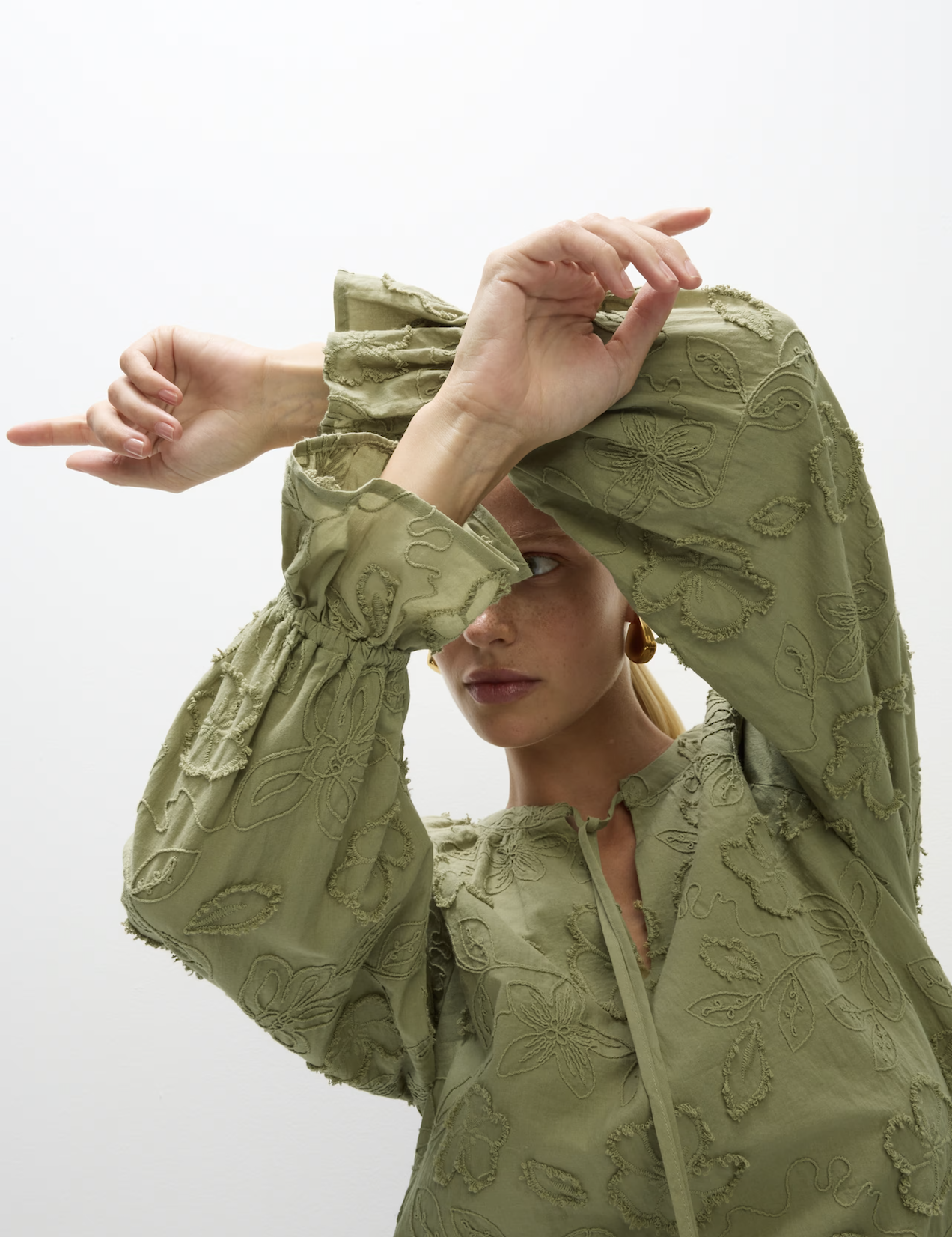 A woman wearing a khaki green appliqué blouse