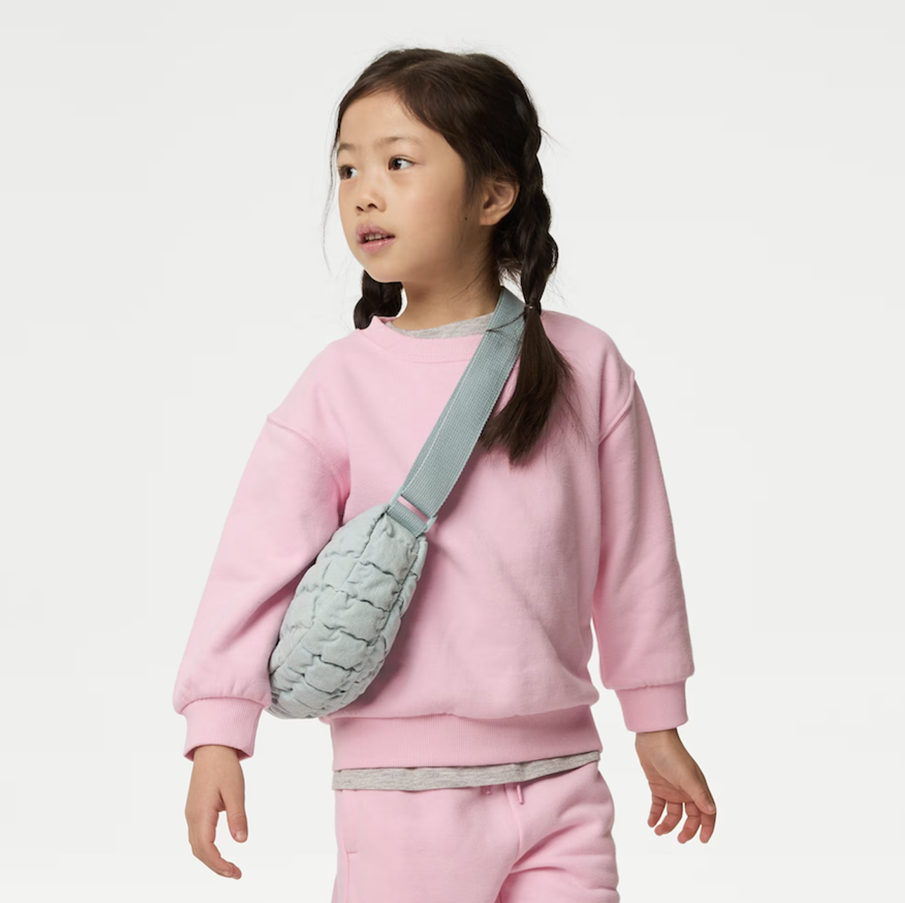 A child wearing a light pink top and carrying a grey cross-body bag